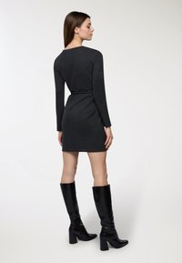 Abito a maglia grigio antracite con silhouette aderente, maniche lunghe e vita cinte da una cintura. Abbinato a stivali neri lucidi sopra il ginocchio.