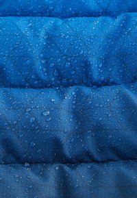 Tissu bleu résistant à l'eau avec une texture matelassée. Les gouttes de pluie perlent visiblement à la surface, mettant en évidence ses propriétés déperlant.