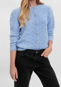 Ljusblå stickad kofta med ett strukturerat mönster, med rund hals, långa ärmar och fem stora grå knappar på framsidan.