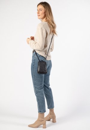 Beige knit sweater, blue denim jeans, and beige heeled boots. Black crossbody bag with strap, smooth texture, rectangular shape.