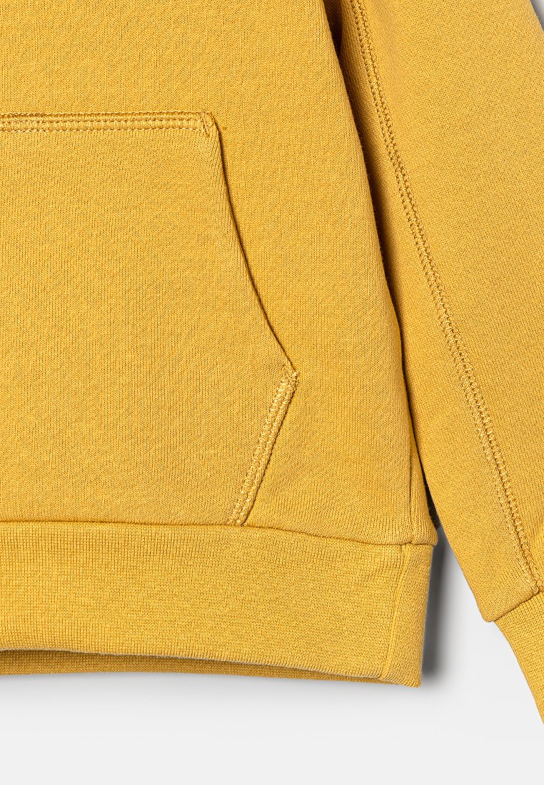 Sweatshirt jaune avec une poche avant, un ourlet côtelé et un tissu texturé. Les coutures sont visibles le long des bords pour une touche de détail supplémentaire.