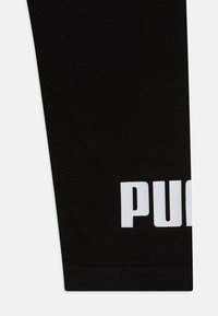 Čierne športové legíny vyrobené z mäkkej zmesi bavlny. Obsahujú výrazné biele logo pozdĺž dolnej časti nohy, majú priliehavý strih a pletenú textúru.