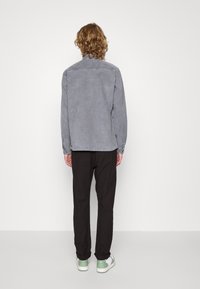 Jacketa din denim gri cu o croială lejeră, mâneci lungi și detalii ale buzunarelor din față, asortată cu pantaloni negri și adidași cu accente verzi.