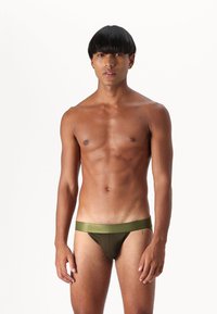 Olivgröna bikini-liknande simbyxor med en slät, glänsande midja. Tyget verkar lätt och åtsittande med minimal täckning.