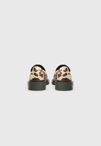Cow-patterned shoes with a cream and brown texture, featuring a round toe, low black sole, and a smooth finish.