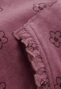 Paarse fleece stof met bloemenpatroon in donkerbruin. Heeft een gerimpelde rand met contrasterende stiksels. Zachte textuur, warme uitstraling.