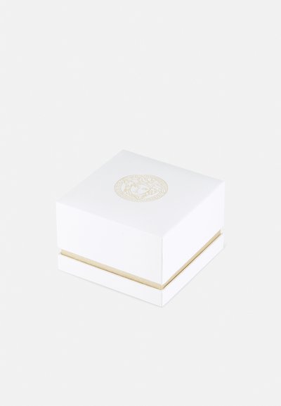 Balts kvadrāts ar zelta dekoratīvu emblemu uz vāka un zelta akcenta joslu ap pamatni. Gluda tekstūra, minimālisma dizains.