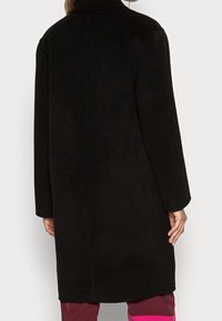 Cappotto nero in lana con taglio dritto, maniche lunghe e collo a revers. Tessuto liscio, dettagli minimali e design a lunghezza media.