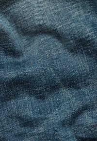 Tela de mezclilla azul oscuro con una superficie texturada, que presenta un desvanecimiento sutil y un patrón de sarga clásico. Textura suave y ligeramente elástica.