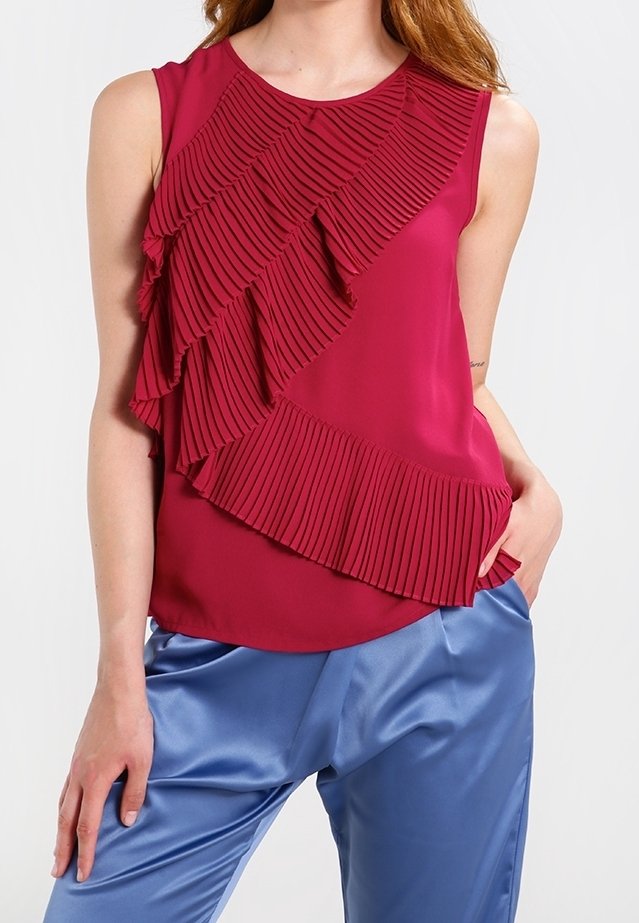 Bezramínkový top v hluboké burgundské barvě s diagonálním skládáním a volánem přes přední stranu; hladká tkanina; doplněný lesklými modrými saténovými kalhotami.