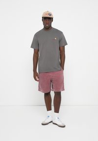 Gray cotton t-shirt with a small logo, paired with dusty rose corduroy shorts. White sneakers and a beige baseball cap complete the look.