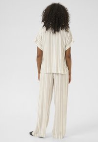 Haut rayé beige et crème à manches courtes associé à un pantalon large assorti, présentant une coupe décontractée et une texture de tissu légère.