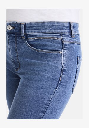 Blaue Jeans aus Denim haben eine schmale Passform mit einer glatten Textur, einem Fünf-Taschen-Design und kontrastierenden Nähten an den Säumen.