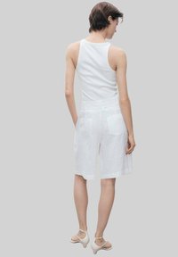 Shorts en lin blancs avec deux poches arrière, associés à un débardeur blanc. Le vêtement a une coupe décontractée et une texture lisse.