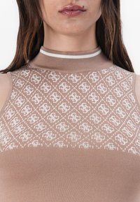 Débardeur en tricot de couleur marron clair avec un motif blanc. Présente un col montant à côtes et une texture lisse sur l'ensemble.
