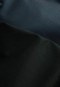 Twee stoffen secties: één marineblauw met een glad, gestructureerd weefsel en één zwart met een matte afwerking, beide van dichtbij.