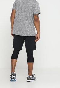 Camicetta corta a maniche corte grigia con texture, pantaloni corti neri e leggings neri. Footwear presenta un design a più motivi con una suola ammortizzata.