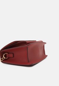 Borsa a mano in pelle rossa con una texture liscia, base piatta e dettaglio in catena dorata. Il design presenta un'ampia apertura per facilitare l'accesso.
