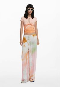 Světle růžový slim fit top s předním výklenkem a zavazováním. Plynulé široké kalhoty s pastelovým tie-dye vzorem v oranžové, zelené a krémové barvě.