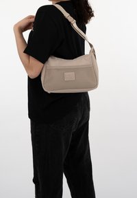 Beige axelväska med texturerad meshpanel, justerbar rem, dragkedja och en liten logotypmärke. Slätt tyg med strukturerad form.