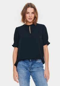 Blusa blu navy con maniche a palloncino corte e scollatura a chiave, realizzata in un tessuto morbido, abbinata a jeans in denim azzurro chiaro.