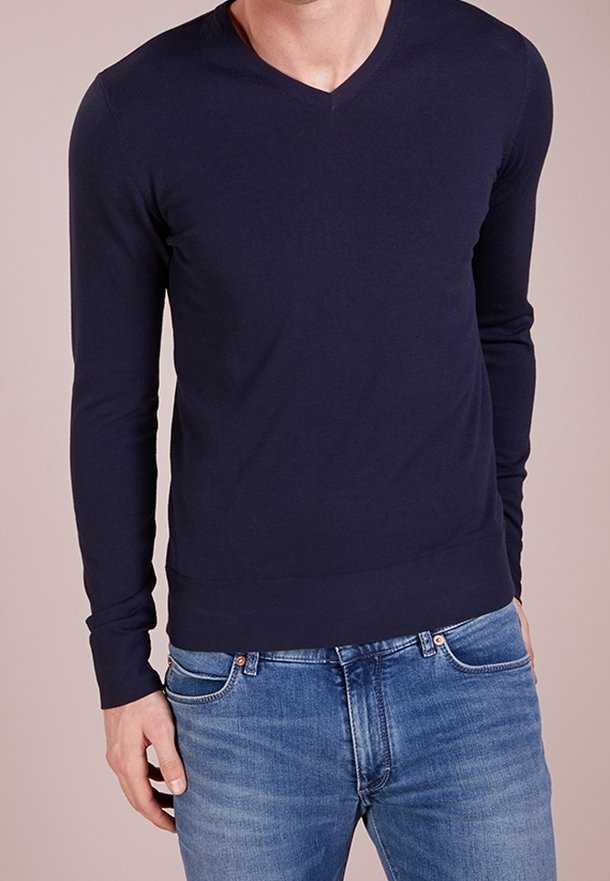 Pull col en V à manches longues bleu marine en tissu doux, coupe ajustée, assorti à un jean en denim bleu clair. Pas de logos ni motifs visibles.