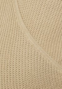 Tissu tricoté beige clair avec une texture lâche, présentant un accent de couture diagonale et un bord côtelé lisse et robuste.