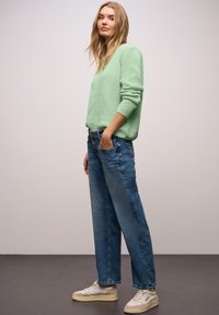 Světlý zelený svetr s texturou kombinovaný s volně střiženými, vybledlými modrými džíny a béžovými teniskami. Jednoduchý design, ležérní styl.