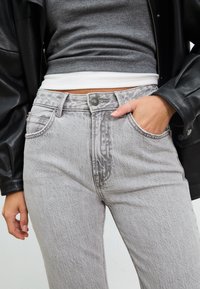 Svijetlosivi traperice s visokim strukom, s dizajnom od pet džepova i suptilnom izbljeđelom teksturom. Završene metalnim gumbom i kontrastnim šavovima.