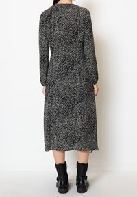 Schwarz-weißer, gepunkteter Midikleid mit langen Ärmeln, rundem Ausschnitt und lockerem Schnitt, kombiniert mit schwarzen Combat Boots.