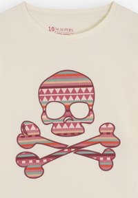 Camiseta de algodón en color crema, con un diseño de calavera estampada en rosa, rojo y verde azulado, y huesos cruzados debajo.