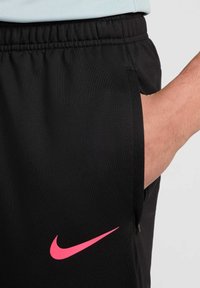 Juodi sportiniai šortai su elastinga juosmens juostele, su rožiniu Nike logotipu kairėje pusėje ir šonine kišene su užtrauktuku.
