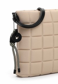 Borsa a tracolla beige imbottita con superficie testurizzata, tracolla in pelle nera e cordone intrecciato decorativo con un'etichetta circolare nera.