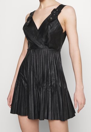 Czarna sukienka bez rękawów ze skóry, z plisowanym dołem, dekoltem w kształcie litery V oraz regulowanymi paskami z klamrami na ramionach.