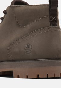 Brown waterproof suede boot with thick rubber sole, detailed stitching, and a pull tab at the back for easy wear.