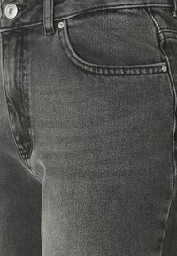 Jeans de mezclilla negra con una vista en primer plano de la textura de la tela, con un bolsillo frontal y un detalle de botón de metal visibles.