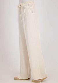 Wijde broek in lichtbeige stof met een elastische tailleband en zijzakken. Gladde textuur en losse pasvorm voor comfort.
