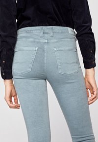 Jeans ajustados de color azul claro con una textura suave, que cuentan con dos bolsillos traseros y una cinturilla de altura media. Mostrados desde una vista trasera en ángulo.