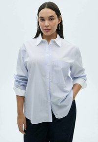 Camicia button-up a righe blu chiaro con colletto, maniche lunghe arrotolate fino ai gomiti e taschino sul petto. Tessuto liscio e vestibilità comoda.