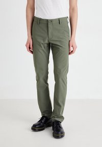 Olive green cotton trousers with a straight fit, front button closure, belt loops, and side pockets, paired with black lace-up shoes.