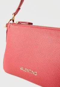 Punane tekstuuriga nahast käekott kuldse tõmbluku ja reljeefse "VALENTINO" logoga. Omadusena eemaldatav rihm mitmekülgsuse tagamiseks.