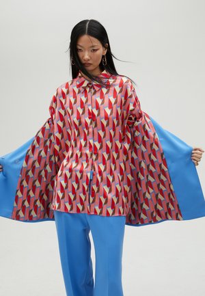 Camisa roja y azul con estampado de formas geométricas, hecha de tela brillante. Combinada con pantalones de pierna ancha en azul sólido.