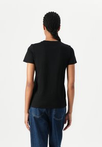 Svart kortermet t-skjorte laget av bomull, med klassisk rund hals og en fitted design, kombinert med blå denim jeans.