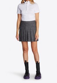 Top blanco de manga corta con cuello con volantes y detalle de botones, combinado con una falda plisada a cuadros negros y botas negras hasta el tobillo con suelas moradas.