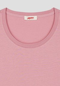 Camiseta de algodón rosa con cuello redondo, que presenta un ribete acanalado y una etiqueta roja con "JOTT" en la parte posterior del cuello.