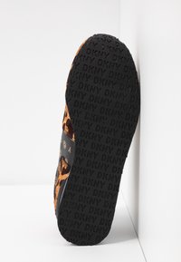 Chaussure DKNY avec une semelle en caoutchouc noir texturé, présentant un dessus en imprimé léopard orange et marron avec des accents de logo subtils.