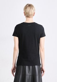 Melns kokvilnas T-krekls ar īsām piedurknēm, apaļu kakla izgriezumu un smalku raibumu tekstūru. Iedarbina neliels logo tuvumā kakla aizmugurē.