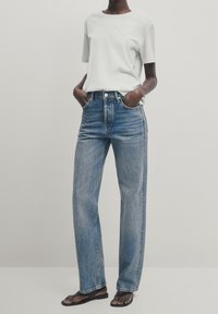 Vitt kortärmat T-shirt parat med ljusblå högmidjade raka jeans, med en urtvättad look och mörka sömmar. Platta sandaler.