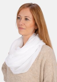 Étole blanche, légère, avec une texture douce et transparente, drapée en plusieurs couches autour du cou, complétant un pull en tricot beige.