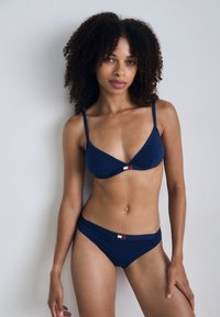 Ensemble de bikini bleu marine comprenant un haut triangle avec des bretelles ajustables et un fermoir à l'avant, associé à un bas de bikini taille basse.